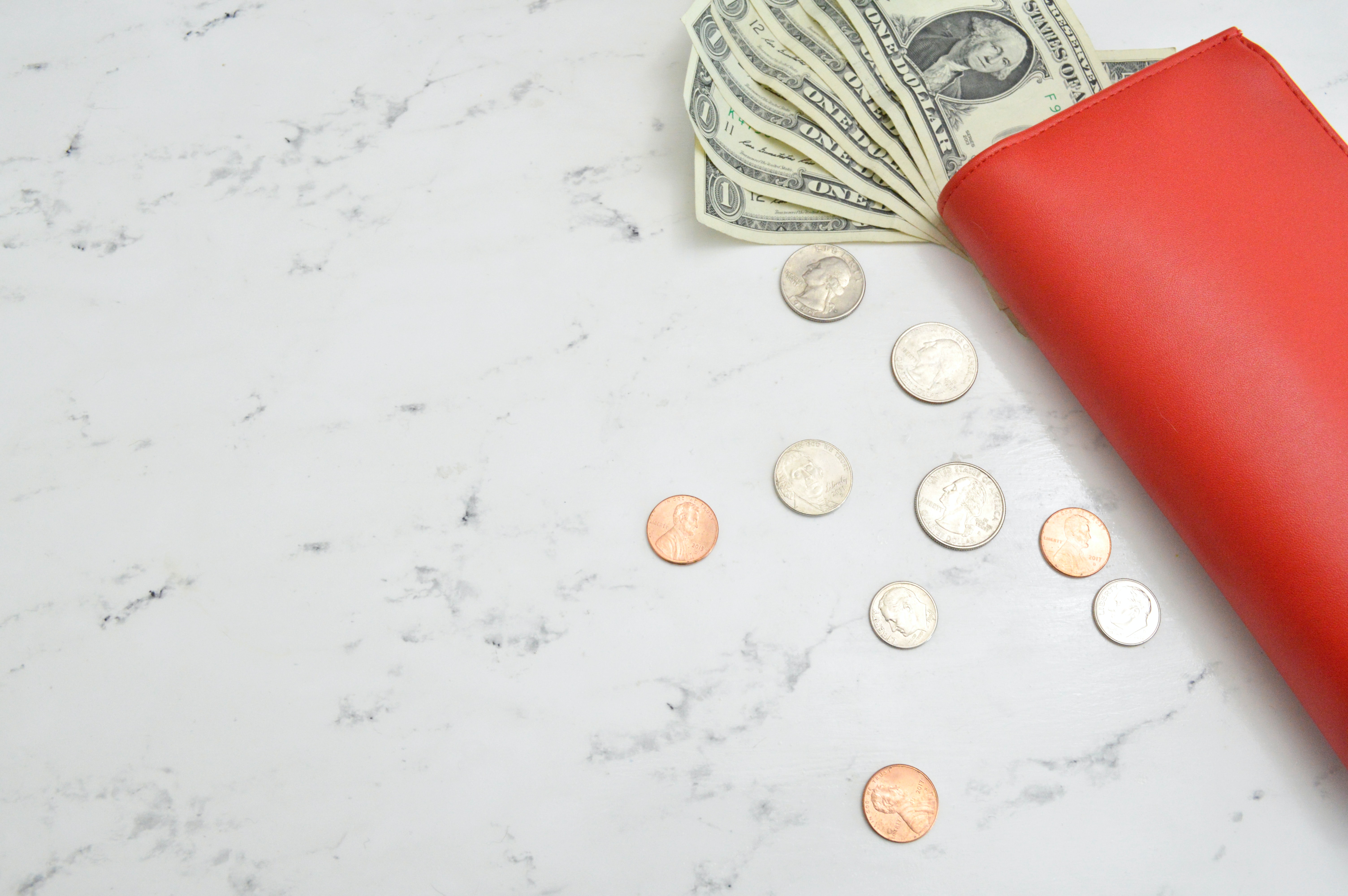 Dollar Bills and Coins on Marble Surface with Red Wallet