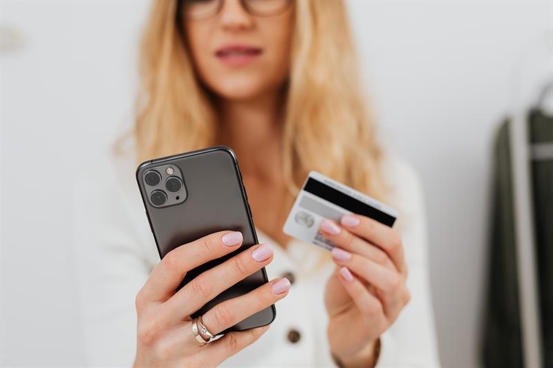 Debit Card VS Credit Card: Which One is Right For You? Woman Holding Phone and Debit/Credit Card