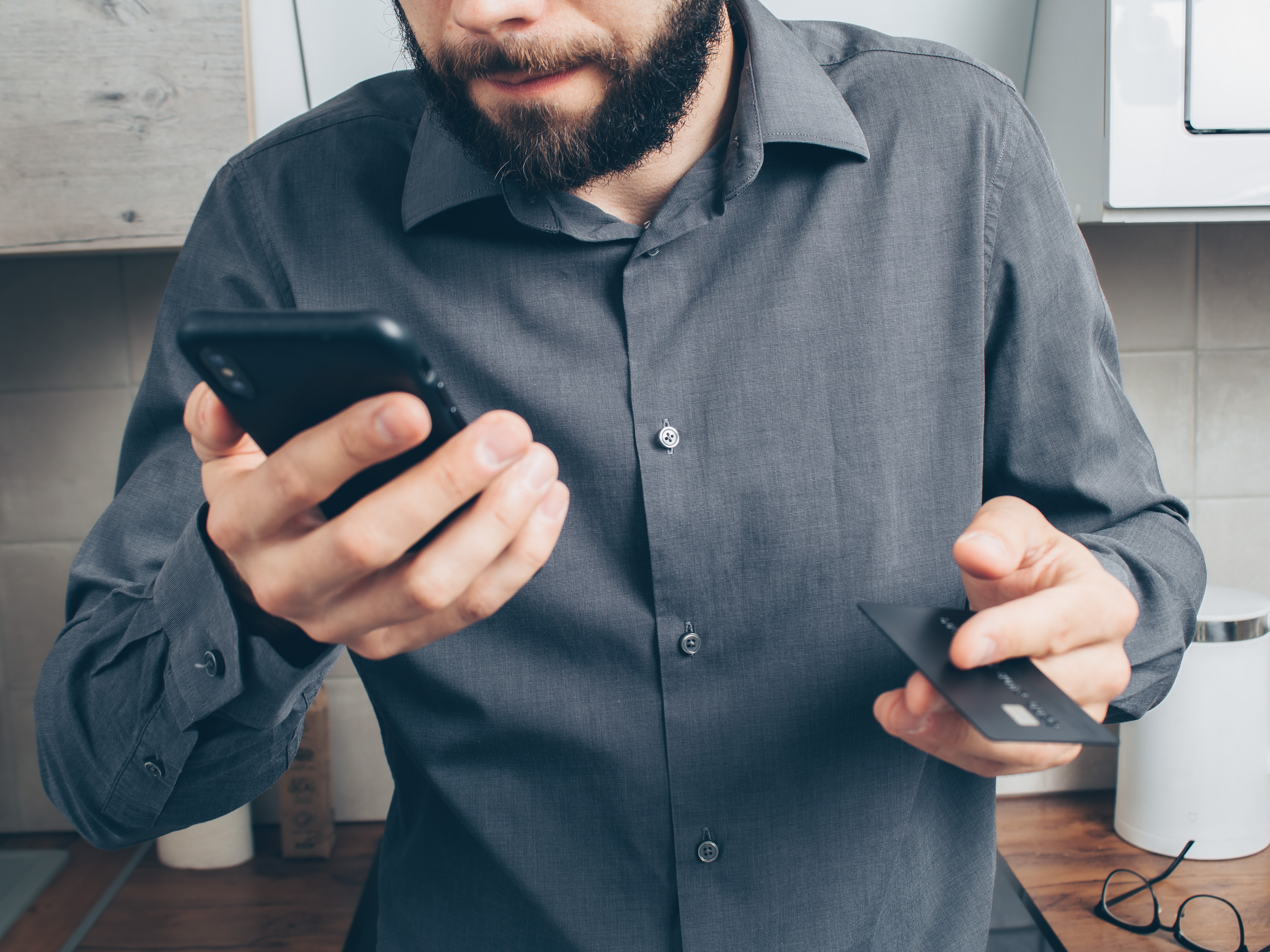 Man Holding Debit Card and Phone with Shocked Look