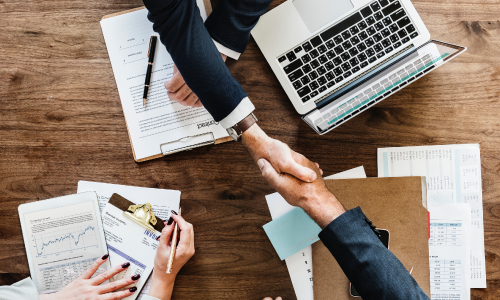 benefits Headshake Across Table with Laptop and Papers