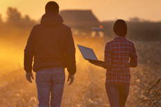 Man and Woman Walking through Field with Laptop in Hand